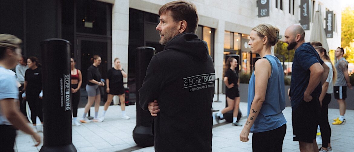 Tipps vom Coach - August Edition. Gruppe beim Outdoortraining HEAVYBAG. Teilnehmer im Vordergrund trägt SECRETBOXING Hoodie.